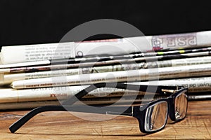 Folded pile newspapers with a pair of blue reading glasses on it