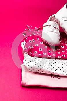 Folded pink bodysuit with shoes on it on minimalistic pink background. diaper for newborn girl. Stack of infant clothing. Child ou