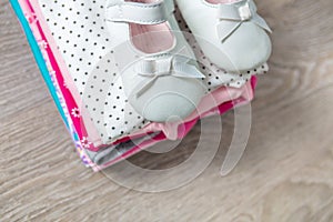 Folded pink and white bodysuit with shoes on it grey wooden background. diaper for newborn girl. Stack of infant clothing. Child