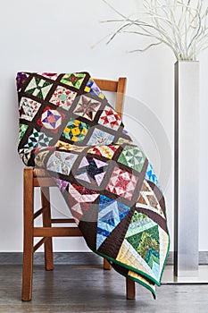 Folded quilt on a chair and floor lamp against a neutral wall