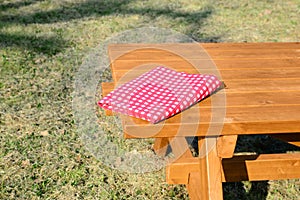 Folded red and white checkered tablecloth on wooden picnic table in park