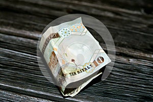 Folded Saudi Arabia money of 10 SAR ten riyals isolated on wooden background, Crumpled 10 Saudi Riyals cash bill banknote