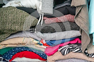 Folded sweaters and garments of a woman`s wardrobe in a closet. Depicting excess, the need for closet organization, tidyin