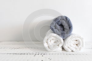 Folded two white and one grey towels on a white wooden table. Spa and wellness, cotton terry textile. Ecological theme