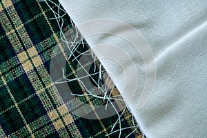 Folded white fabric with frayed edge on top of green plaid