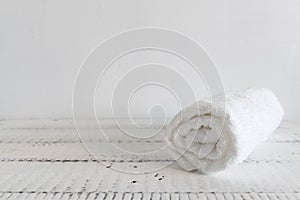 Folded white towel on a white wooden table. Spa and wellness, cotton terry textile. Ecological theme.