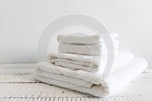 Folded white towels of different sizes on a white wooden table. Spa and wellness, cotton terry textile. Ecological theme