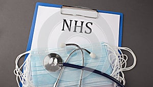 Folder with paper text NHS , on a table with a stethoscope and medical masks, medical concept