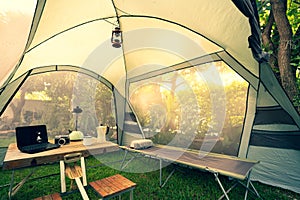 Folding bed inside the tent in the morning Oil lamps and coffee sets, notebooks on a wooden camping table and outdoor ideas