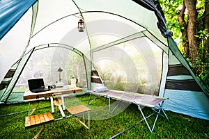 Folding bed inside the tent in the morning Oil lamps and coffee sets, notebooks on a wooden camping table and outdoor ideas