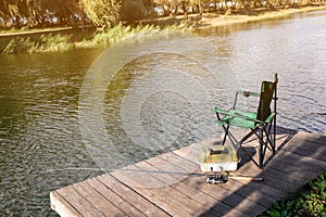 Folding chair, tackle box and rod for fishing on wooden pier at riverside.