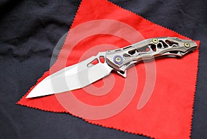 Folding knife stainless steel sharp blade gray titanium handle close up still life red background