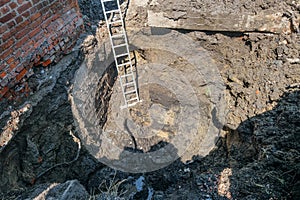 Folding metal ladder installed in a dug pit to inspect the foundation of a building