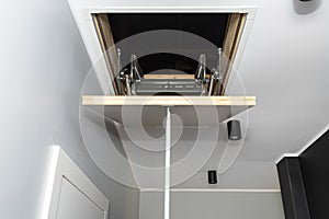 Folding metal stairs to the attic in the ceiling, closed hatch with a tube for opening, modern look.