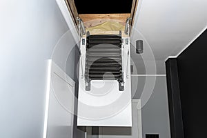 Folding metal stairs to the attic in the ceiling, open hatch and complex stairs, modern look.