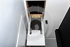 Folding metal stairs to the attic in the ceiling, open hatch and complex stairs, modern look.