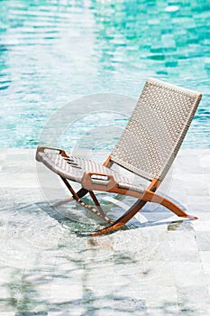 Folding rattan chair chaise longue by the pool. Clear transparent water