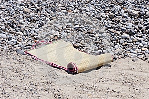 A folding straw beach mat on the shingle. Beach, lay down.