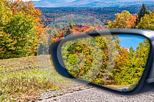 Foliage colors in fall season. Rural road in the autumn with yellow, brown and red colored trees reflected in car mirror