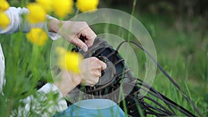 Folk crafts. Handmade. Young woman weaves rattar baskets sitting in the grass. Yellow flowers in the foreground