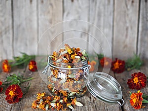 Folk medicine.Glass storage jar with medicinal dried red flowers of black marigolds on a wooden background.The benefits of