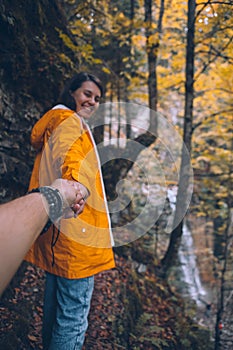 follow me concept woman in yellow raincoat walking by trail to forest waterfall