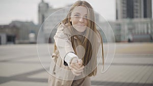 Follow me concept. Young beautiful woman stretching hand to camera. turning and walking along city square. Portrait of