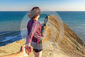 Follow me. Hand in hand. Teen tourist girl standing on mountain cliff against beautiful landscape of sea, cape and sky in sunny