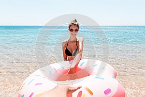 Follow me Vacation concept. girlcalls to swim in the sea and waves her hand. Girl relaxing on inflatable ring in the sea. Summer