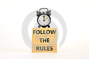 Follow the rules symbol. Concept words Follow the rules on wooden blocks. Beautiful white background. Black alarm clock. Business