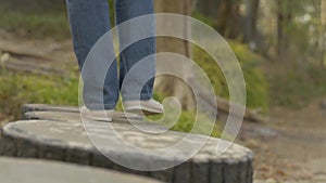 Follow shot from rear back of woman legs wearing jeans walking leisurely on concrete stump in natural park during summer.