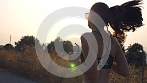 Follow to sporty girl jogging in country road. Young woman in sunglasses running outdoors and listening music from