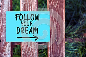 Follow Your Dreams inspirational life quote text written on paper on a fence