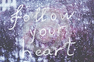 Follow your heart, written by hand on the snowstorm winter background, toned