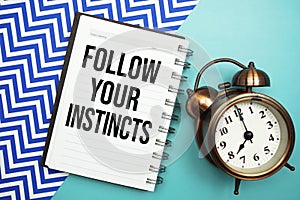 Follow Your Instincts text written on notepad with alarm clock