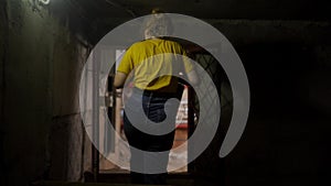 Following back shot of female plumber in dark basement heading to boiler room. Woman engineer walks through underground