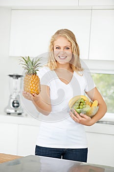 She follows a balanced diet. Curvaceous young woman holding up fresh fruit in her kitchen.