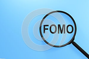 FOMO acronym, Fear of Missing Out on magnifier isolated on blue background
