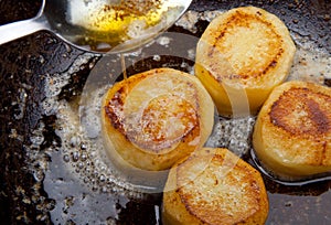 fondant potato frying in sauce pan. butter basting food with spoon whilst cooking. gourmet restaurant dish