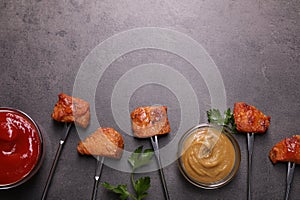 Fondue forks with pieces of fried meat and sauces on grey table, flat lay. Space for text