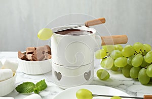 Fondue pot with dark chocolate and grapes on  table