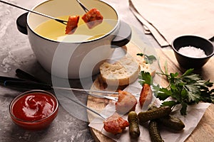 Fondue pot, forks with fried meat pieces, ketchup and other products on grey textured table