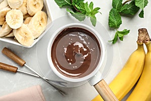 Fondue pot milk chocolate and bananas on light table, top view