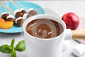 Fondue pot with milk chocolate on light table,