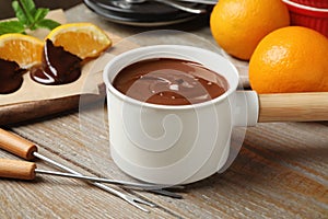 Fondue pot with milk chocolate and oranges on wooden table