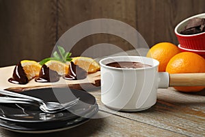 Fondue pot with milk  and oranges on wooden table