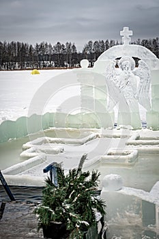Font for dipping into an ice hole for the baptism of christ and ice sculpture in the form of an angel and a cross