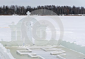 Font for dipping into an ice hole for the baptism of christ and ice sculpture in the form of an angel and a cross