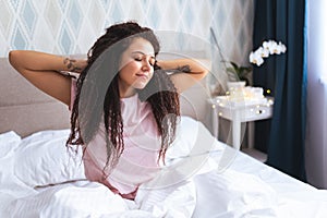 Font view of young woman waking up in early morning sitting on bed with whitesnow linen and sretch her arms and body