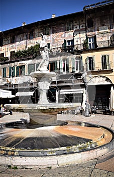 Fontana Madonna Verona, in the foreground with the frescoed and sunlit facades of ancient buildings in Piazza delle Erbe in Verona photo